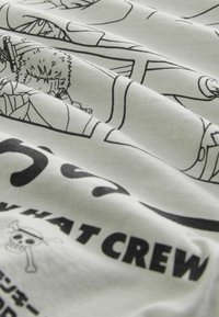 Hvid bomulds T-shirt med sorte trykte illustrationer og tekst. Funktioner karakterer fra tegneserier og pirattema grafik. Glat tekstur, rynket.