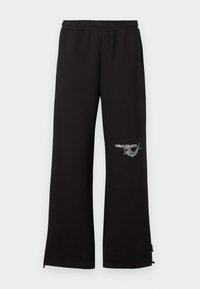 Black sweatpants with an elastic waistband, featuring an embroidered logo and graphic detail on the left leg. Straight-leg cut with zippers at hems.