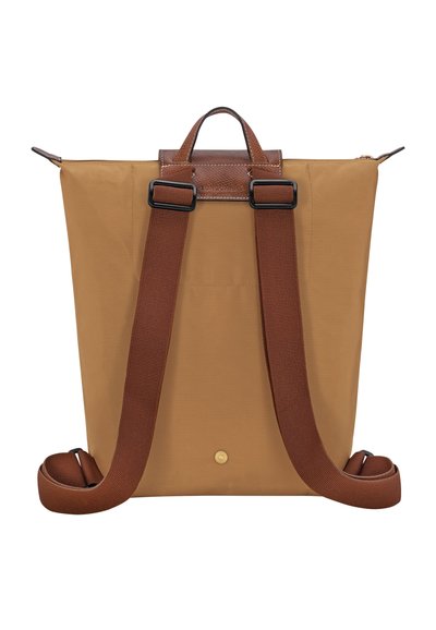 Tan fabric backpack with brown leather accents, top handle, and adjustable straps. Smooth texture with a minimalist design.