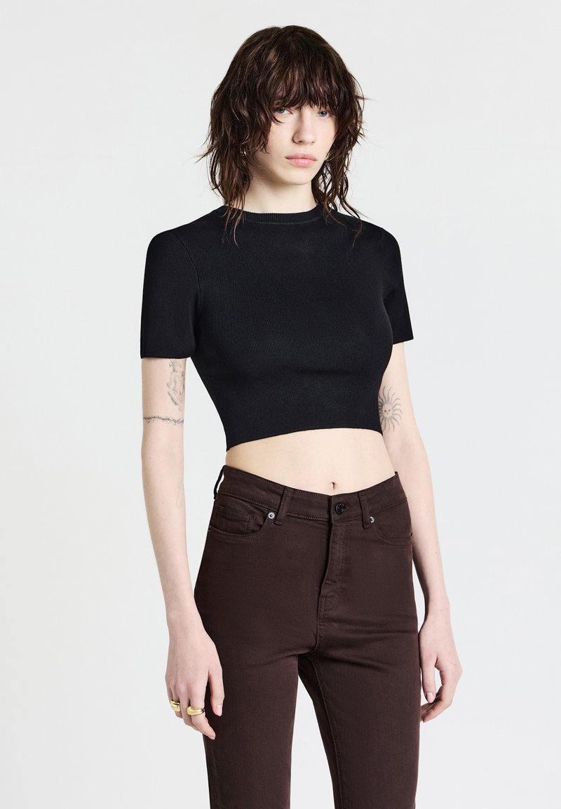 Top corto nero a maniche corte, realizzato in tessuto a coste, abbinato a jeans fitted marrone scuro con chiusura a bottone classica.