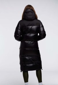 Zwarte pufferjas met een capuchon, voorzien van een glanzende, doorgestikte textuur en verticale baffels. Inclusief branding op de bovenrug. Middenlange uitvoering.