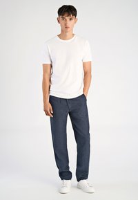 Biała koszulka z krótkim rękawem w parze z luźnymi granatowymi spodniami z teksturowanym wzorem, dopełniona białymi trampkami. Prosty i nowoczesny design.