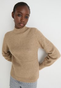Beige ribbed knit sweater with a mock neck and long sleeves, featuring a soft texture and a fitted silhouette.
