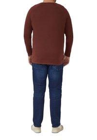 Braunes Langarmshirt mit Raglanärmeln, kombiniert mit dunkelblauen Jeans und hellen Schuhen. Klassischer, lässiger Schnitt und Stil.