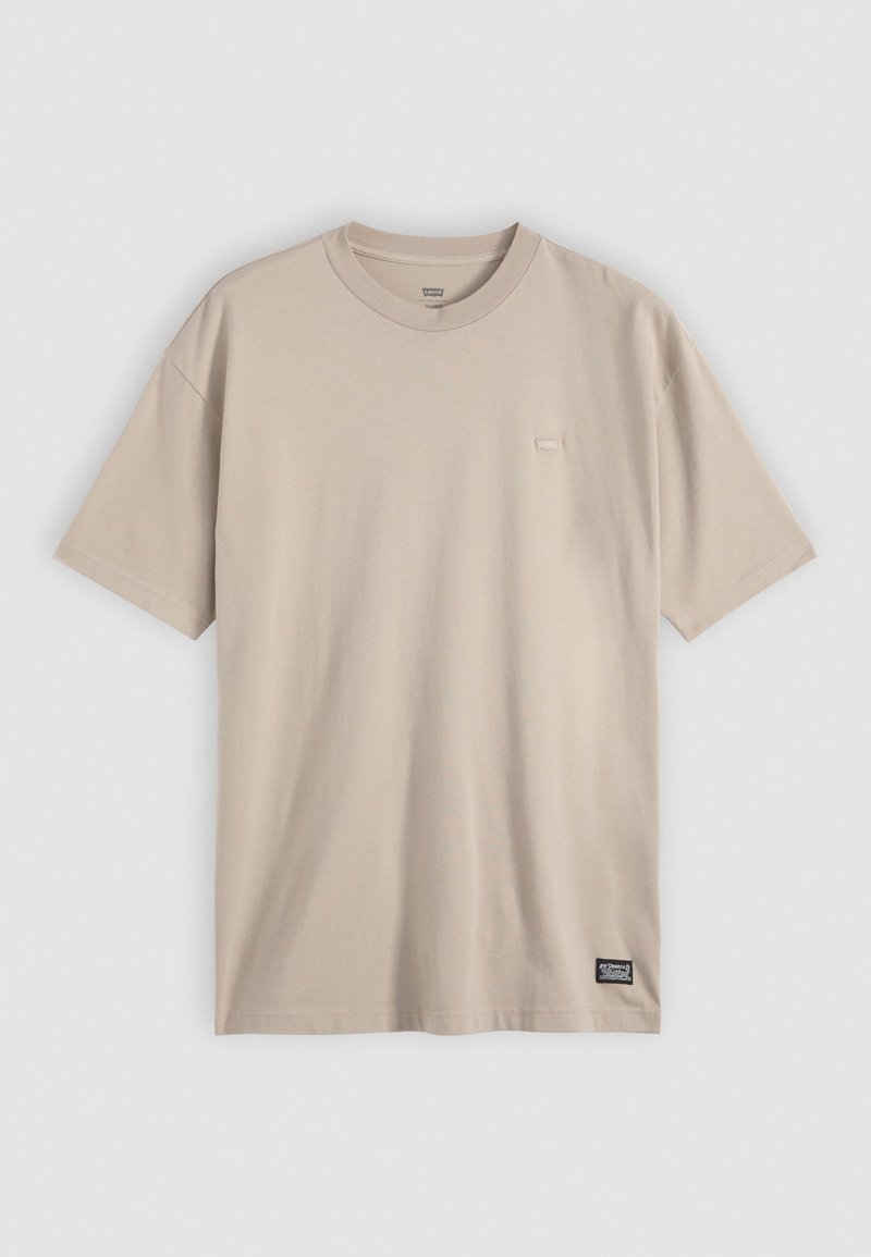 Beige T-Shirt mit kurzen Ärmeln aus weichem Baumwollmaterial. Verfügt über einen runden Halsausschnitt und ein kleines Markenetikett an der unteren linken Seite. Glatte Textur.