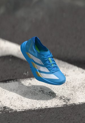 Chaussure de course légère en bleu vif avec des accents blancs et dorés. Elle présente un design respirant et une semelle texturée pour une meilleure adhérence, flottant au-dessus d'une piste.