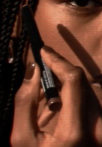 Schwarzer Eyeliner-Stift, der zwischen den Fingern gehalten wird, mit glatter Textur und glänzender Spitze. Die Haut hat einen warmen Farbton mit sorgfältig manikürten Nägeln.