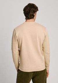 Sudadera beige de manga larga, con cuello redondo y puños acanalados, confeccionada en tela suave. Presenta un diseño liso sin patrones.