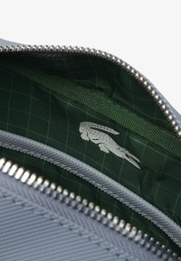 Borsa grigia con chiusura a zip e superficie liscia. L'interno presenta una fodera a quadretti verdi e un logo stampato. Hardware della zip in argento.