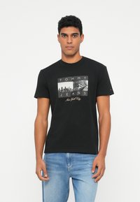 Must musta T-särk, millel on grafitootena New Yorgi pilt ja tekst "TOMMY JEANS". Lühikesed varrukad, ümmargune kaelus, mugav lõige.