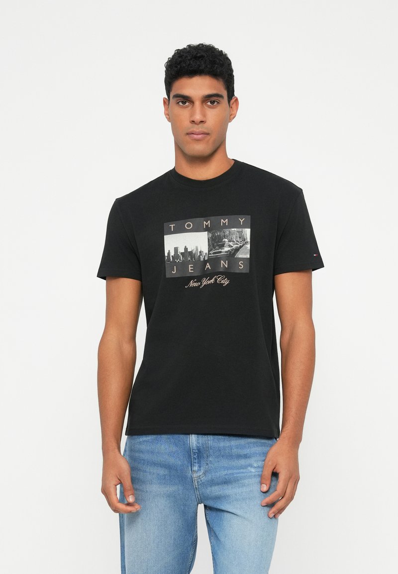 Must musta T-särk, millel on grafitootena New Yorgi pilt ja tekst "TOMMY JEANS". Lühikesed varrukad, ümmargune kaelus, mugav lõige.