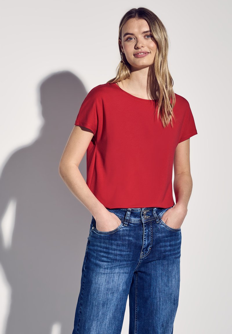Top rosso a maniche corte con scollatura rotonda, abbinato a jeans in denim blu a vestibilità comoda con tasche frontali e design classico a cinque tasche.