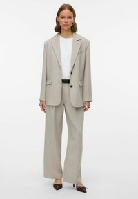 Vaaleanharmaa puku, jossa on yksirivinen takki, jossa on leikatut läpät ja leveälahkeiset housut, yhdistettynä valkoiseen t-paitaan ja ruskeisiin korkokenkiin.