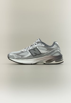 Szürke és fehér New Balance futócipő hálós és bőrből készült anyagokkal, vastag párnázott talppal és fűzős kialakítással, oldalnézet semleges háttéren.