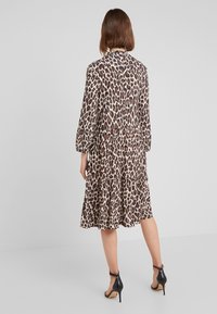 Leopardenmuster-Kleid mit langen Ärmeln, gestuften Design und leichtem Stoff. Kombiniert mit schwarzen High-Heel-Sandalen.