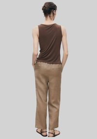 Top marrone senza maniche, pantaloni in lino color marrone chiaro, vestibilità comoda, e vista posteriore. L'outfit è completato da sandali flat.