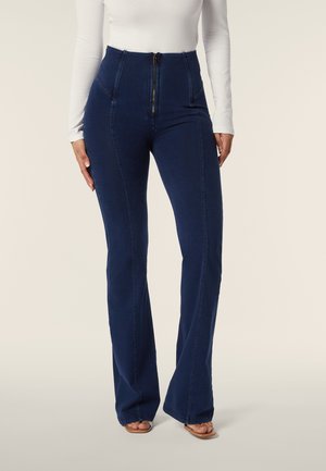 Jeans a vita alta svasati in denim blu scuro. Presentano una chiusura con zip frontale, tasche laterali e cuciture a contrasto lungo le cuciture.