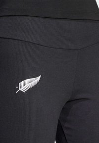 Leggings neri a coste con un logo di felce bianco sul lato sinistro in basso, dotati di una cintura elastica liscia per il massimo comfort.