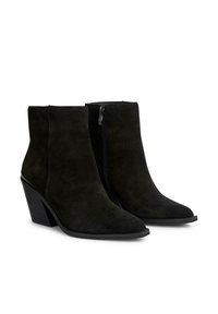 Botas de ante negras hasta el tobillo con puntera afilada, tacón cónico y cierre lateral de cremallera. Textura suave con un acabado mate y una altura modesta.