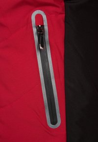 Tissu de veste rouge et noir avec une poche zippée bien visible. La fermeture éclair est en argent avec une tirette texturée et soulignée en gris.