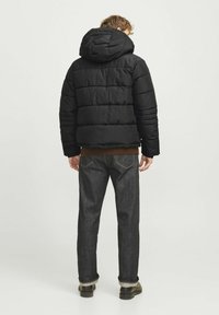 Sort pufferjakke med hætte, der har horisontale quiltede sektioner. Sammen med mørk denimjeans og sorte støvler, set fra ryggen.