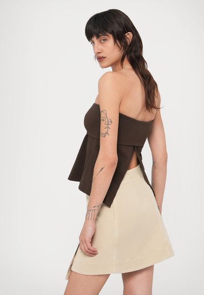 Καφέ, τοπ χωρίς τιράντες με σχέδιο πεπλούμ και πλαϊνή σκίσιμο, συνδυασμένο με εφαρμοστή μπεζ μίνι φούστα. Λείο ύφασμα, μινιμαλιστικό στυλ.