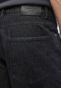 Κοντινό πλάνο στην πίσω τσέπη μαύρου τζιν από denim με δερμάτινη ετικέτα μάρκας «Mads Nørgaard Copenhagen» πάνω από την τσέπη.