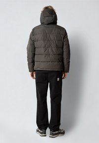 Polstret mørkegrøn jakke med hætte, der har et quiltet design. Bæres med sorte bukser og sneakers. Minimalistisk stil, ingen synlige logoer.
