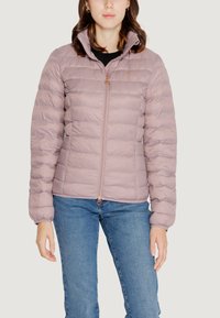 Giacca a vento di colore lilla con zip frontale, cuciture orizzontali, colletto alto e un piccolo logo. Indossata sopra una maglietta nera e jeans blu.