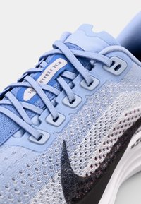 Chaussure de course Nike bleu clair avec une tige en maille, des motifs texturés, des lacets plats et un logo swoosh noir bien en vue.