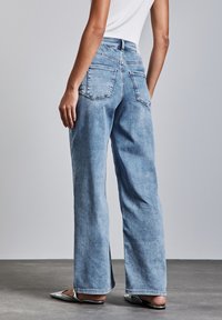 Ljusblåvida jeans med hög midja, som har två bakfickor, en mjuk textur och fransade detaljer vid benänden.