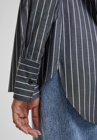 Grijs gestreept overhemd met witte lijnen, met een gebogen zoom en manchette details. Gecombineerd met een denim onderstuk, zichtbaar met stofstructuur.