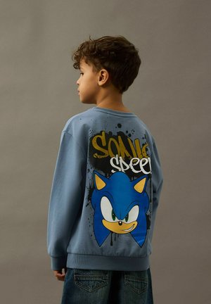 Sinine svett, millel on seljal suur Sonic the Hedgehog'i graafika, kollase aktsentiga ja mustade laigukestega.