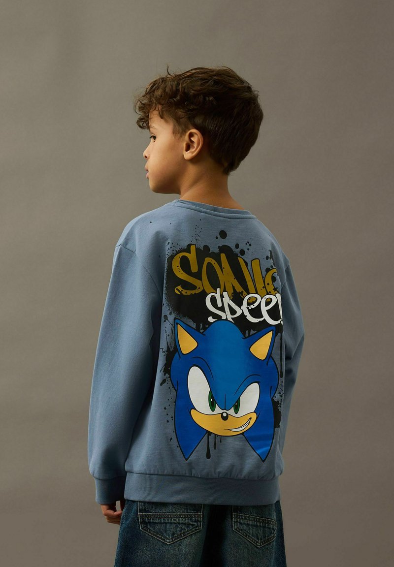 Plava dukserica s velikim grafičkim otiskom Sonica Ježa na leđima, s žutim naglascima i crnim mrljama.