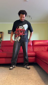 Juodas marškinėliai su spalvinga Nike grafika, vaizduojančia krepšinį ir žaidėją. Derinama su tamsiomis džinsinėmis kelnėmis ir juodai baltais sportbačiais.