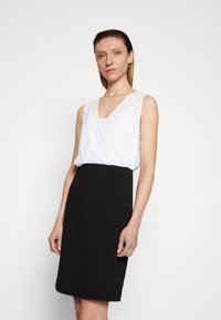 Vestido preto e branco; sem mangas, com decote em V; parte superior branca lisa; parte inferior preta ajustada. Design simples e linhas limpas.