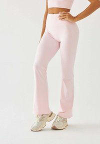 Różowe legginsy dzwony wykonane z elastycznej tkaniny, z wysokim stanem. Połączone z jasnymi trampkami z beżowymi akcentami.