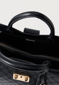 Crna kožna torba s reljefnim uzorkom, zlatnim hardverom, dvostrukim ručkama i unutarnjim džepom sa zatvaračem. Glatka tekstura sa strukturiranim oblikom.