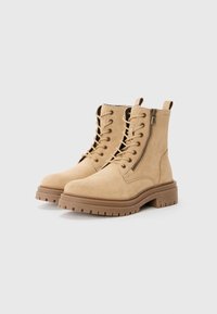 Bottines en suède tan avec une semelle en caoutchouc épaisse, un devant à lacets et un zip sur le côté. Présente des coutures renforcées et un design robuste.