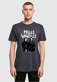 Czarna koszulka z grafiką na przodzie przedstawiającą dwie postacie z napisem "MILLI VANILLI" powyżej. Wykonana z miękkiej bawełny, z okrągłym dekoltem.