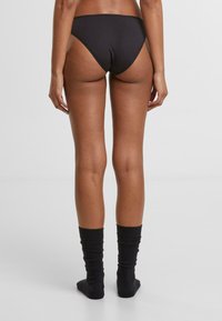 Fekete pamut bikini alsó, magas fazonú hátsó résszel, fekete térd fölé érő zoknival párosítva. Az anyag simának tűnik, minimális varrásokkal.