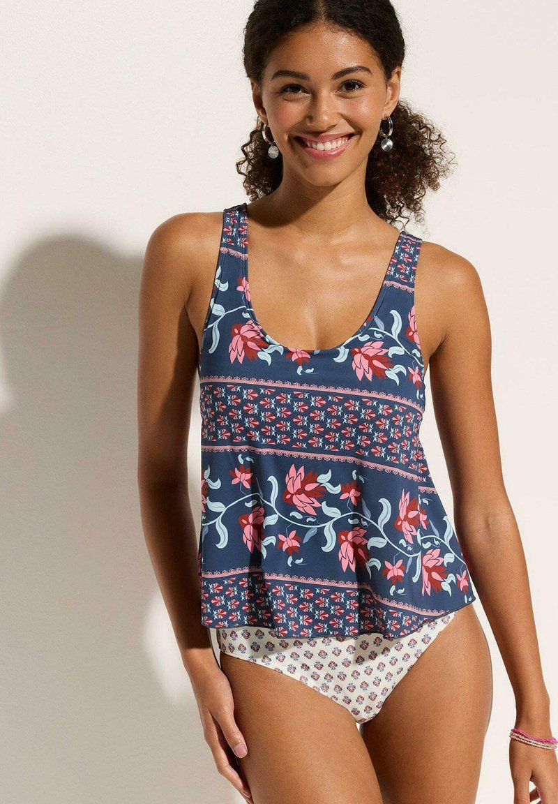 Haut de tankini avec un motif floral marine, ourlet évasé et décolleté rond. Le bas est en tissu crème avec un petit motif floral.