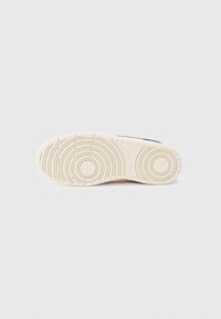 Semelle de chaussure en caoutchouc blanche avec des motifs de traction circulaires et linéaires. Dotée d'une surface légèrement texturée, conçue pour la prise et la durabilité.