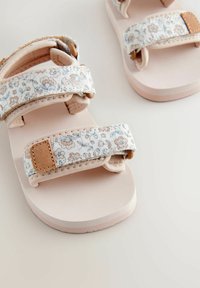 Helle rosa Sandalen mit Stoffriemen im Blumenmuster, verstellbaren Klettverschlüssen und einer glatten, gepolsterten Sohle.