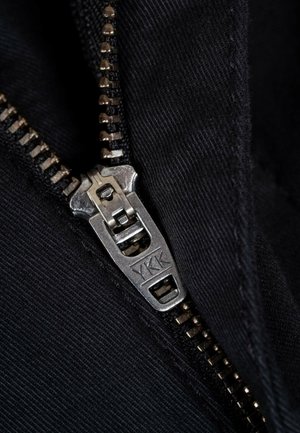 Black fabric featuring a silver metal zipper with a visible YKK logo. Zipper teeth are evenly spaced along the track, indicating high quality.