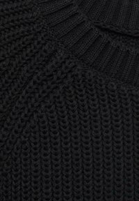 Črna pletena obleka z rebrastim okroglim ovratnikom. Ima gosto, teksturirano vzorčenje z vidno, debelo prejo. Ni dodatnih podrobnosti.