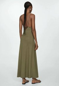 Olivově zelené maxi šaty bez rukávů s otevřeným zadním dílem, zavazováním a splývavou siluetou. Texturovaná látka se elegantně vlní.
