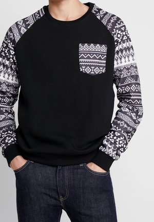Schwarzer Pullover mit gemusterten langen Ärmeln und Taschen, der geometrische Designs in Weiß und Grau auf einem einfarbigen schwarzen Körper zeigt.