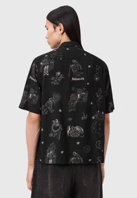 Μαύρο πουκάμισο με κοντά μανίκια που διαθέτει περίπλοκη λευκή κεντητική με διάφορα σχέδια, όπως σκελετούς, φυτά και άλλα μοτίβα.