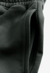 Schwarze Baumwoll-Jogginghosen mit weicher Textur, elastischem Bund und seitlichen Taschen. Nahaufnahme betont die Stoffstruktur.